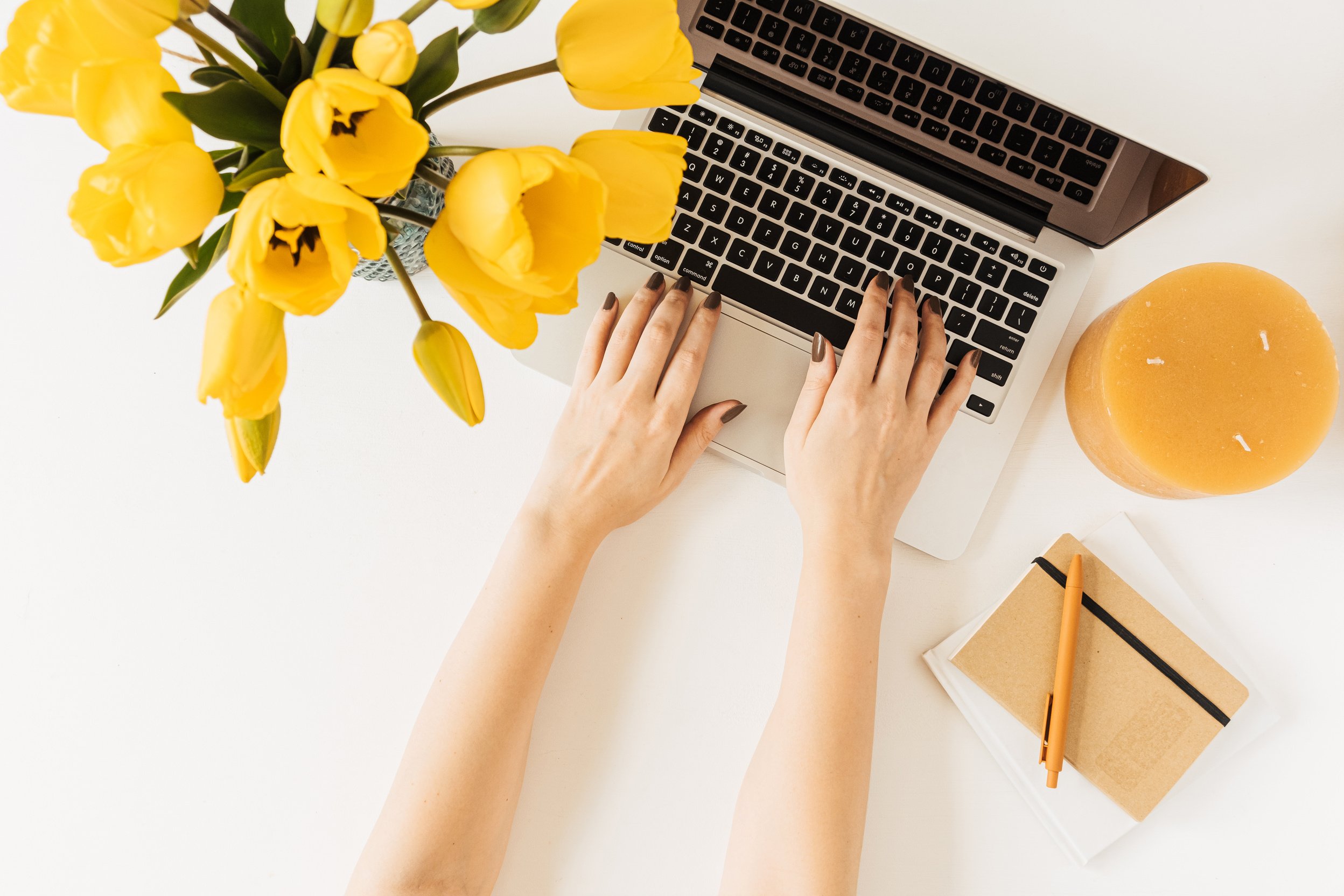 Woman Using Laptop with Flowers and Candles on Desk